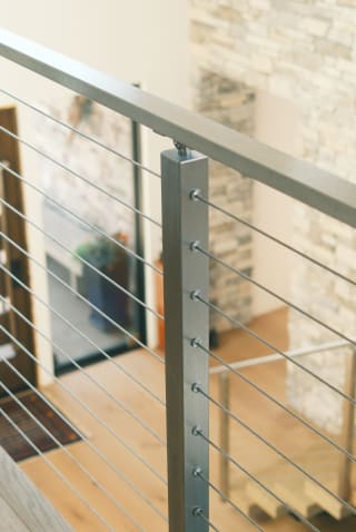 Brushed stainless post and handrail with cable infill above light oak floors.