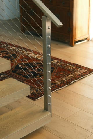 Brushed stainless post with cable infill at the foot of light oak floating treads on a rug.