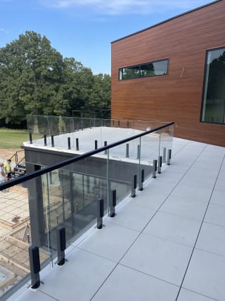 Frameless glass with black talon spigots and handrail wraps a tiled roof terrace beside wood-clad walls