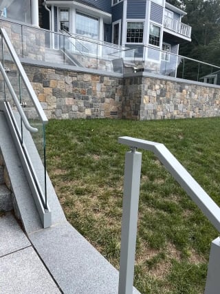 Glass base rail railing follows granite steps up to a stone terrace, with an aluminum post railing in front