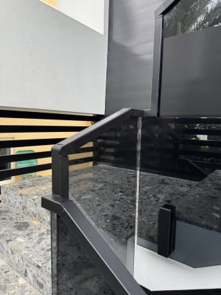 Solar gray tinted glass on side-mounted talons with a black handrail on terrazzo stairs