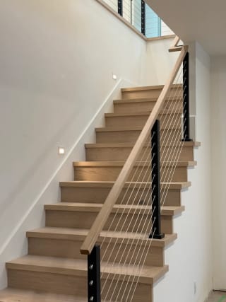White oak stair with a black-post cable railing and continuous oak handrail