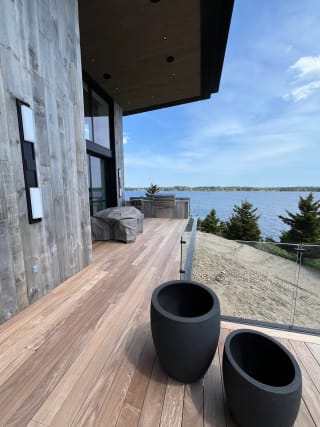 Frameless glass railing on a hardwood side deck with black planters and water beyond.