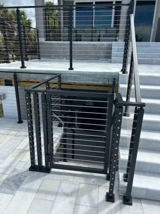A black cable railing gate and posts sit at the base of white marble exterior steps.