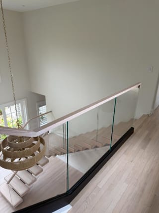 Looking down past a base-rail glass guard with oak handrail onto white-oak floating treads and a woven pendant.
