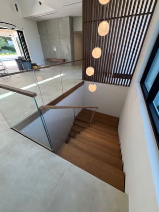 Frameless glass with a walnut top cap wraps a stair opening beneath globe pendants and a wood slat screen