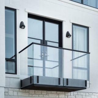 Frameless glass Juliet balcony with black top cap and fascia clamps outside double doors on a white facade.