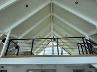 Black rod railing caps a loft balcony beneath a white vaulted ceiling with exposed rafters.