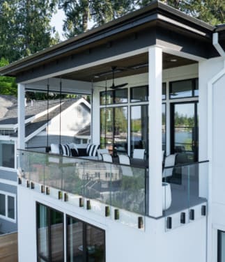 Frameless glass railing held by black side-mounted talon clamps wraps a second-story covered balcony.