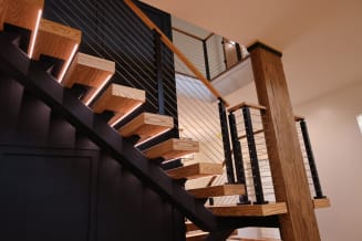 Ash floating treads with LED strips on a black stringer with cable railing and a timber column