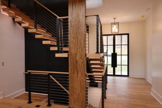 Ash floating switchback stair with black cable railing around a timber column in a bright entry