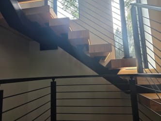 Floating stair with LED-lit treads above a black cable railing at the landing