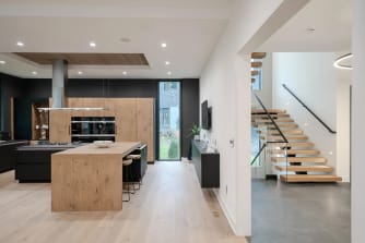 Open modern kitchen leading to an oak floating stair with glass railing and black wall handrail.