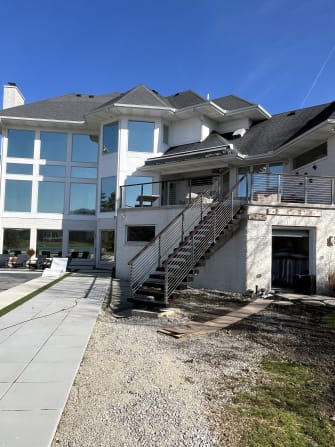 Exterior floating stair with gray cable railing rising to a terrace on a white brick home