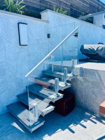 Clear glass panels on Ascend Talon clamps with a stainless top rail follow an outdoor stone-tiled stair.