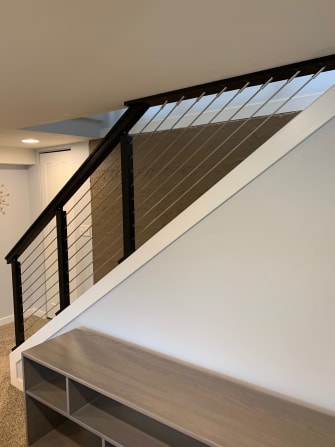 Black cable railing runs above a white knee wall and along a stair opening beside built-in shelving.