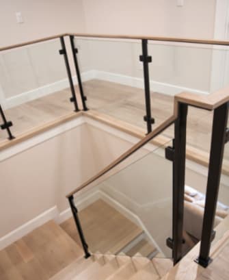 Black posts holding glass panels beneath a continuous light oak handrail wrapping a stair opening.