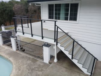 Black cable railing follows a gray exterior stair up to a raised deck beside a pool.