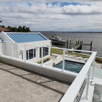 Bright white posts with horizontal rods wrap a rooftop terrace overlooking a pool, docks and bay.