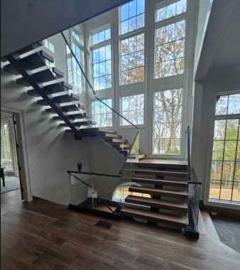Walnut treads on a black mono stringer with frameless glass in a base rail beneath a two-story window wall.