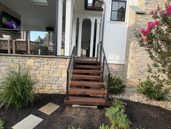 Hardwood steps flanked by black cable railings lead up to a covered porch with matching cable railing.