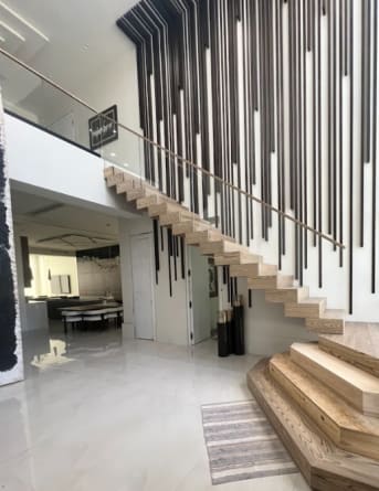 Light oak cantilevered treads rise from stacked plinth steps along a wall of black vertical slats in a glossy white foyer.