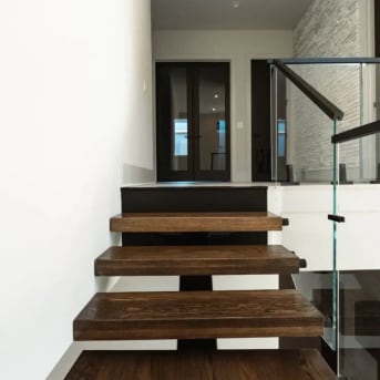 Thick dark-stained floating treads with a frameless glass guard lead to an entry with double doors.