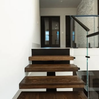 Thick dark-stained floating treads with a frameless glass guard lead to an entry with double doors.