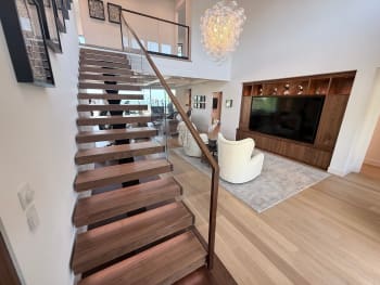 Walnut treads on a hidden mono stringer with frameless glass railing and wood handrail rising into a bright living room.