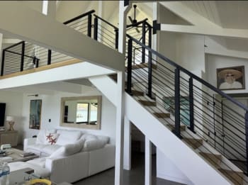 Black rod railing runs up an open white-stringer stair with oak treads to a loft in a bright beach-house living room.