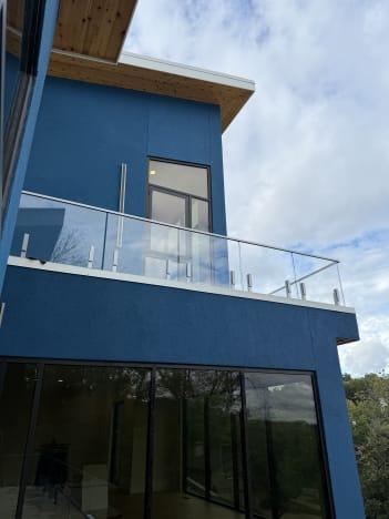 Frameless glass on silver talon spigots wraps a cantilevered balcony on a blue and cedar modern home