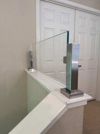 Close view of a brushed stainless post clamping a frameless glass panel atop a white knee-wall cap.