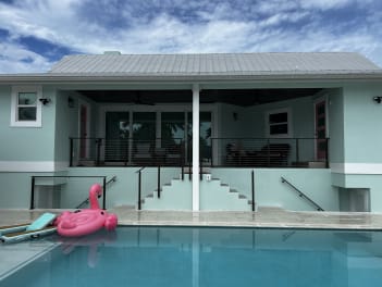 A turquoise home's raised lanai and steps lined with black cable railing above a swimming pool.