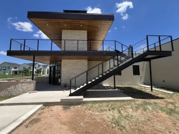 A modern stone-and-stucco home with a cantilevered upper deck and exterior steel stair lined in black cable railing.