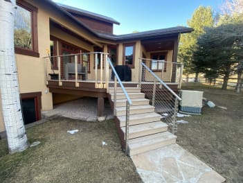 Stucco mountain home with a composite deck stair and stainless cable railing under a blue sky.