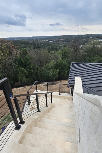 Black cable railing lines curving limestone steps with a wooded hill-country view