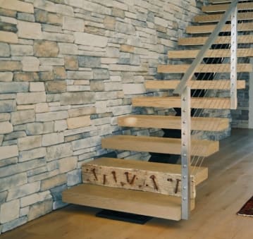 White oak floating treads with stainless cable posts against a stone wall, the first step faced with a reclaimed nail-studded beam.