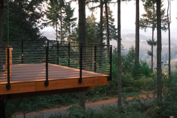 A cedar platform with black side-mount cable railing overlooks a misty forested valley.