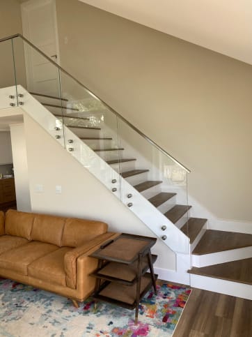 Glass panels on stainless standoff pins with a stainless handrail climb a stair above a leather sofa.