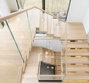 Overhead view of light oak cantilever treads turning at landings with frameless glass and oak handrails under glass pendant lights.