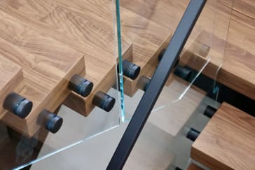 Close detail of black standoff pins securing frameless glass to the edges of thick walnut treads.