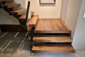 Walnut floating treads step up to a wide walnut landing beside frameless glass railing.