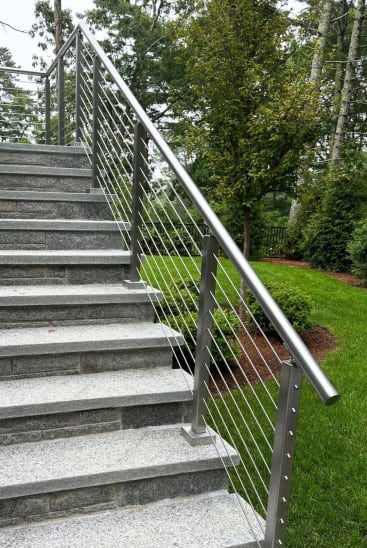 Brushed stainless posts with a 2-inch round handrail and cable infill climbing a long granite garden stair.