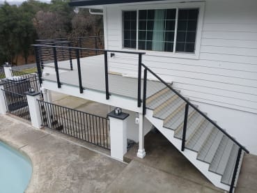 Black cable railing follows a gray exterior stair up to a raised deck beside a pool.