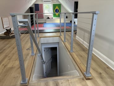 Silver cable railing with an angled stair section surrounds a stair opening in a finished attic room.