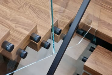 Close detail of black standoff pins securing frameless glass to the edges of thick walnut treads.