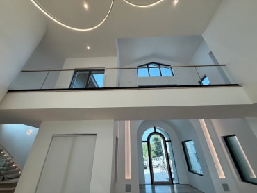 Base rail glass loft railing spans a double-height entry with an arched front door below