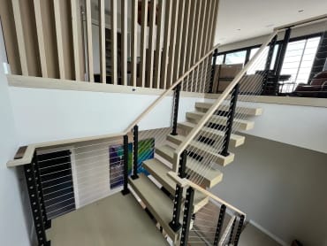 Whitewashed oak FLIGHT Mono switchback with black cable railing and pale oak handrail beside a slat screen
