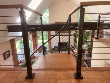 Black posts with wood cap and stainless cables guard a parquet loft beside a curving spiral-stair rail in a vaulted room.