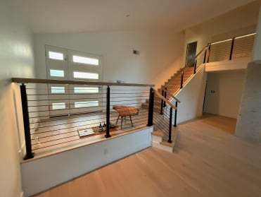 Black aluminum posts with horizontal Onyx rods and a maple cap rail line a split-level entry and stair.